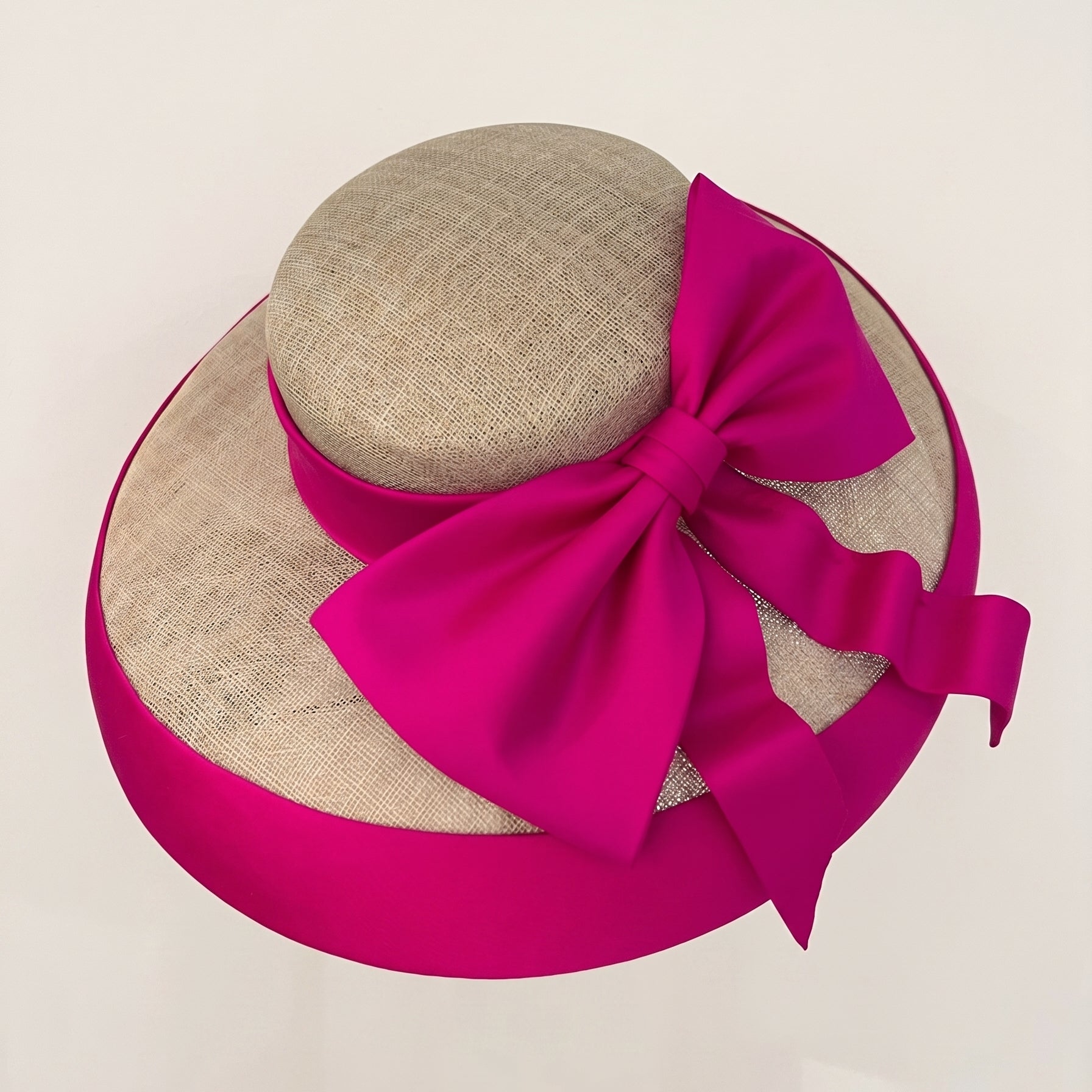 Overhead view of a natural sinamay hat featuring a vibrant fuchsia Dupioni silk bow and brim binding.