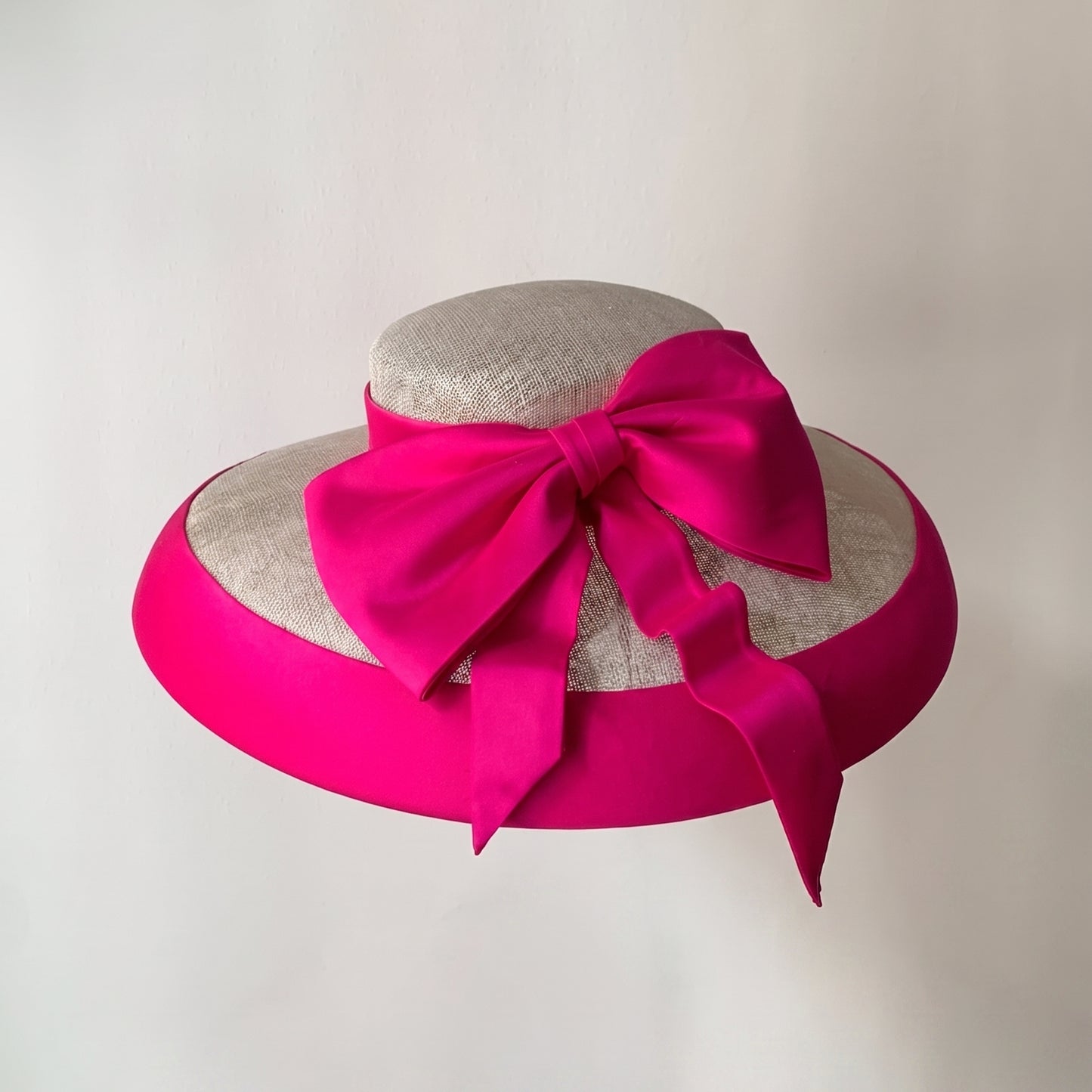 Overhead view of a natural sinamay hat featuring a vibrant fuchsia Dupioni silk bow and brim binding.