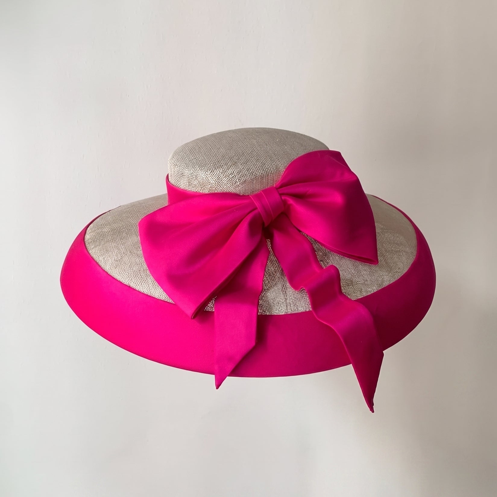Overhead view of a natural sinamay hat featuring a vibrant fuchsia Dupioni silk bow and brim binding.